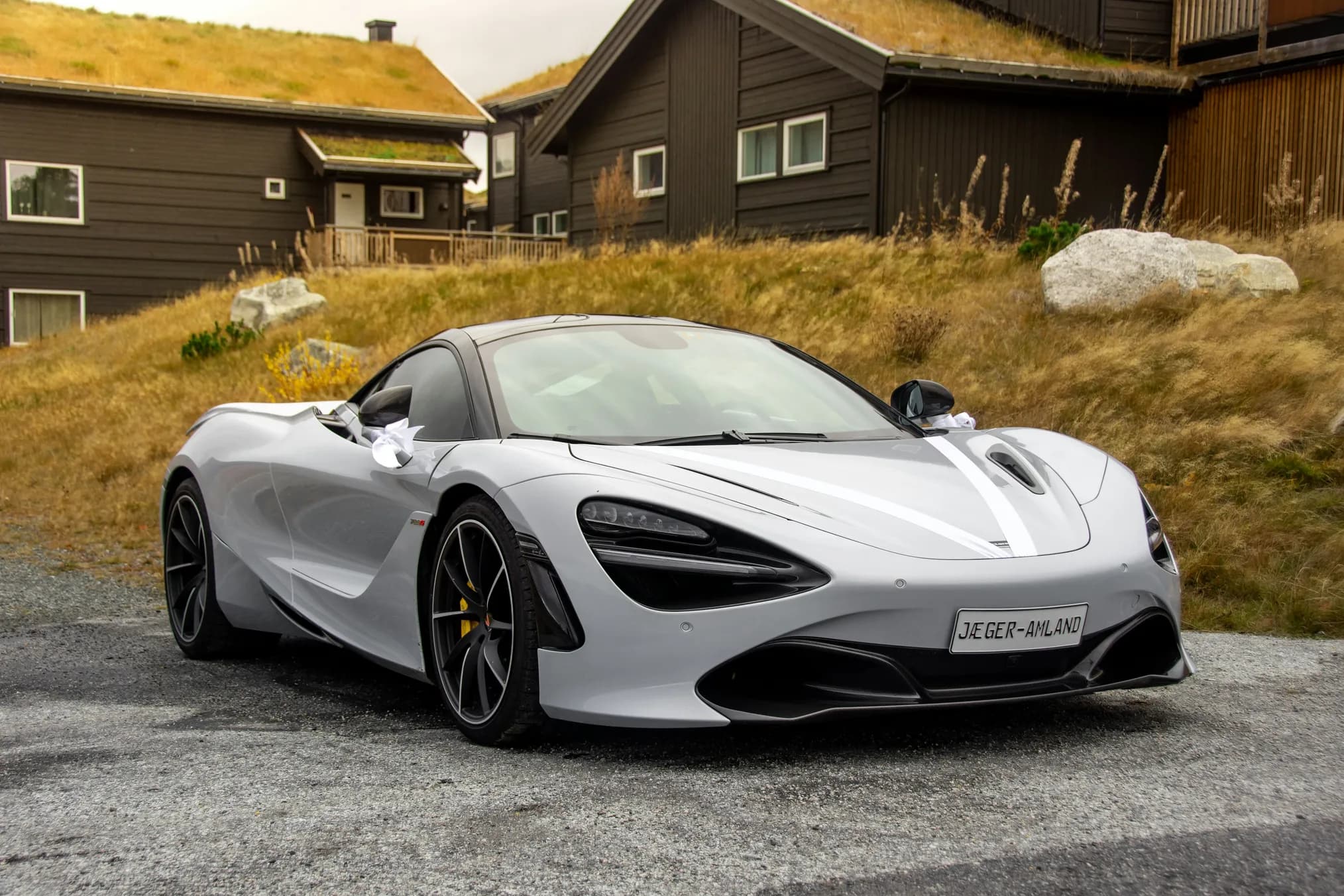 A silver sports car parked below hillside cabins
